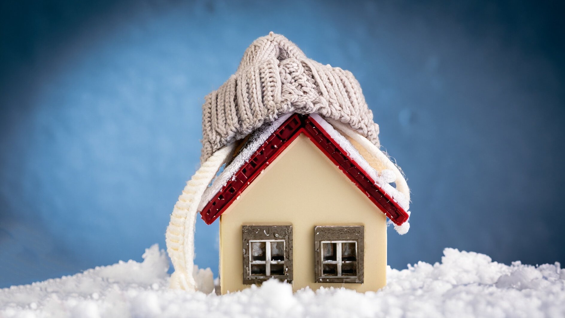 house in winter - heating system concept and cold snowy weather with model of a house wearing a knitted cap